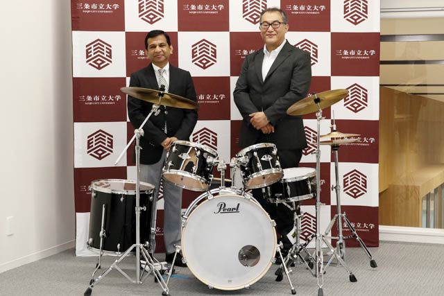 ハードオフコーポレーションが三条市立大学に寄付したドラムセットとシャハリアル学長(左)、原店長