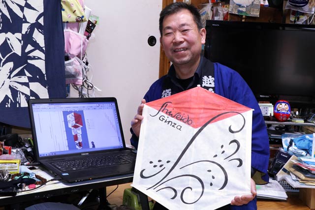 仕事場の須藤さんと作品とパソコンに表示されているのは受注データ
