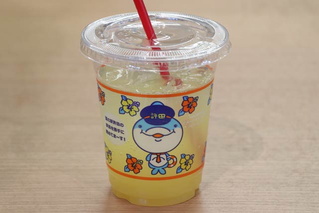 「道の駅 許田」のイメージキャラクター「ピトゥブー」がデザインされたオリジナルカップに入れたシークワーサージュース